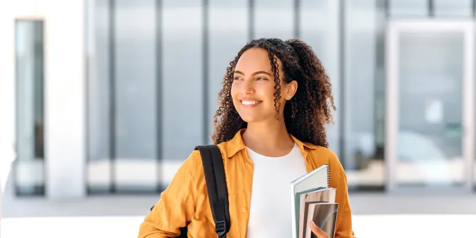 Student wearing backpack and smiling holding textbook